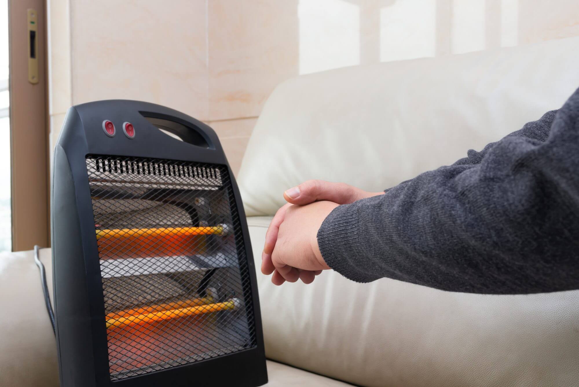 man sitting on sofa with an electric heater near his hands