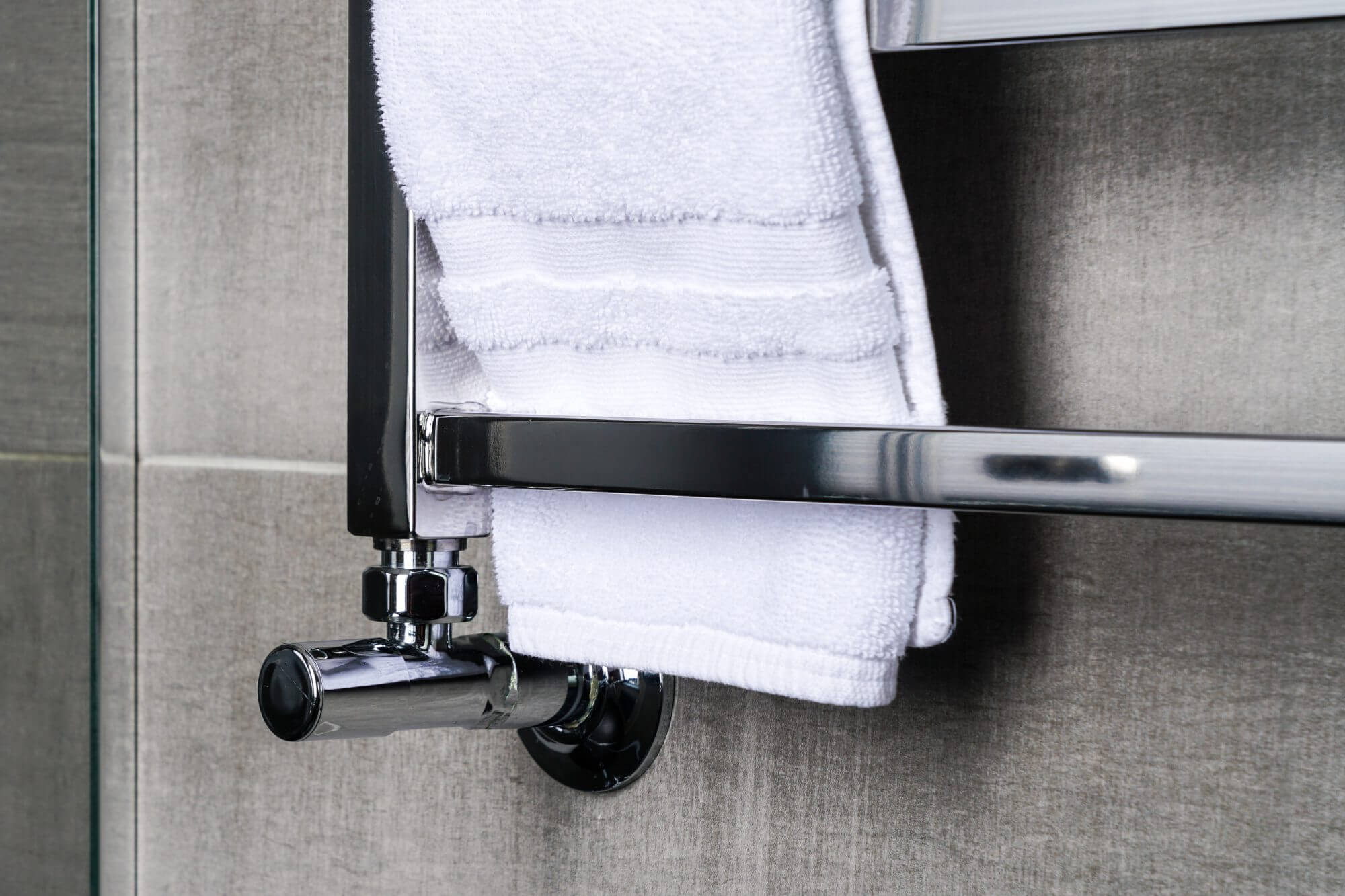 fragment of a modern stainless steel bathroom towel dryer on the gray anthracite tile wall