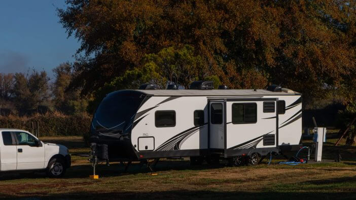 Rv trailer parked under tree with truck for pulling and blue skies