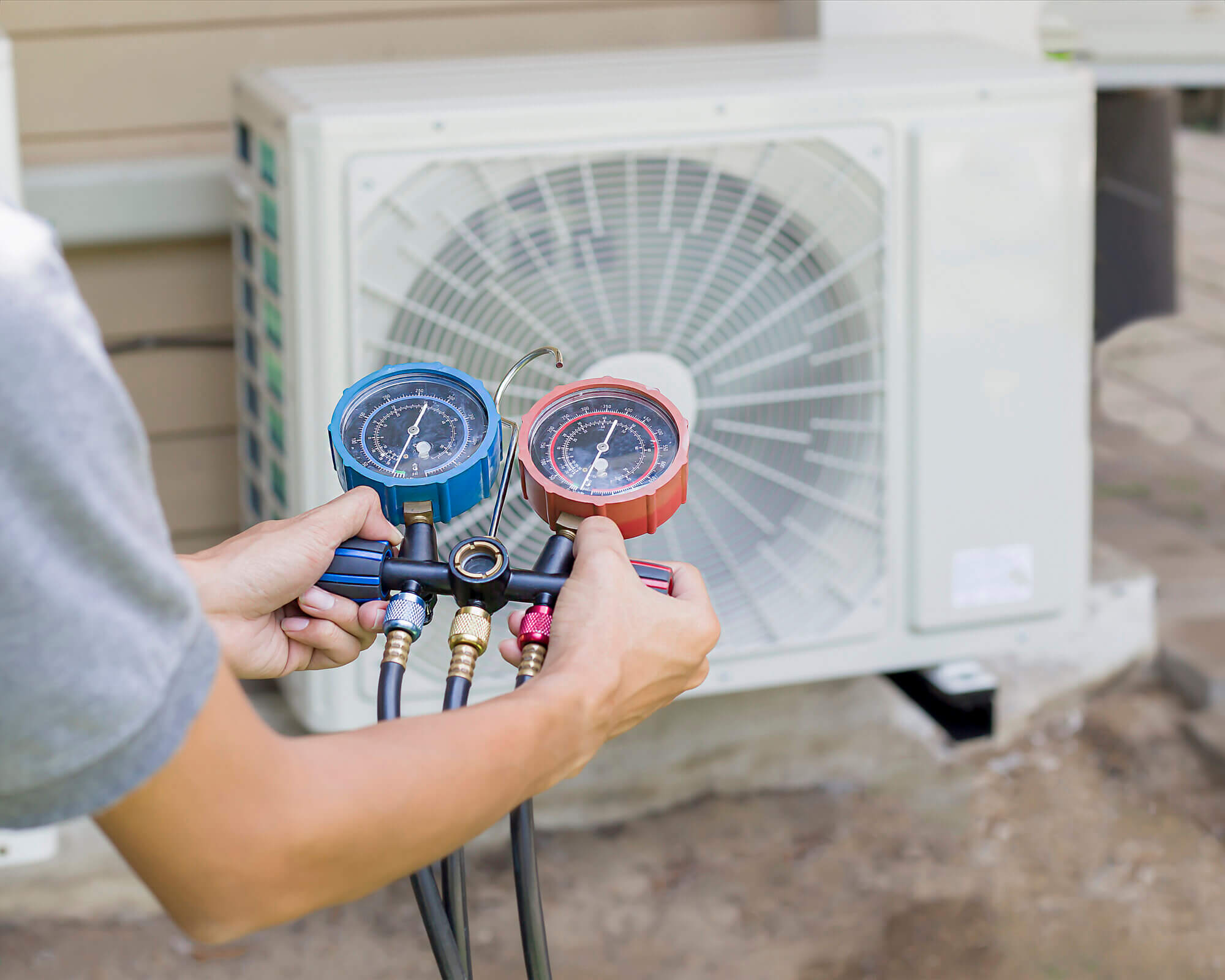 Air repair mechanic using measuring equipment for filling industrial factory air conditioners and checking maintenance outdoor air compressor unit.