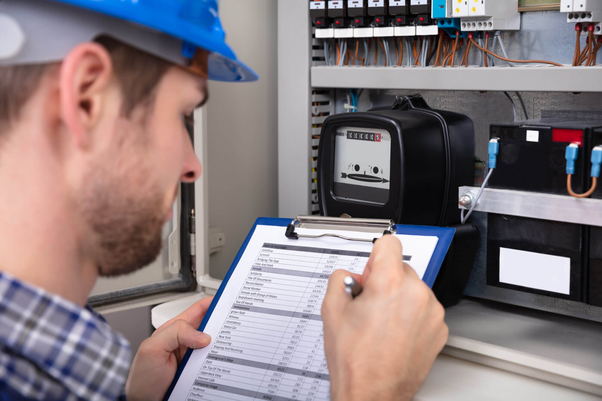 Close-up Of Male Technician Writing On Clipboard In Front Of Fuse Box