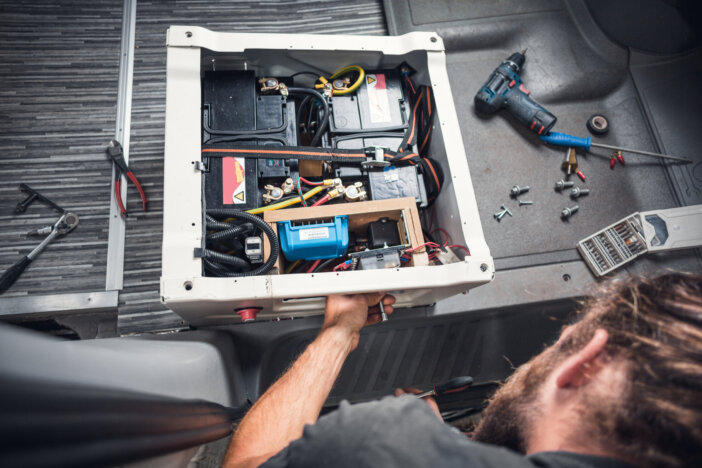 Bearded man working on a DIY camper van. He is working on the base of a front seat to install additional batteries.