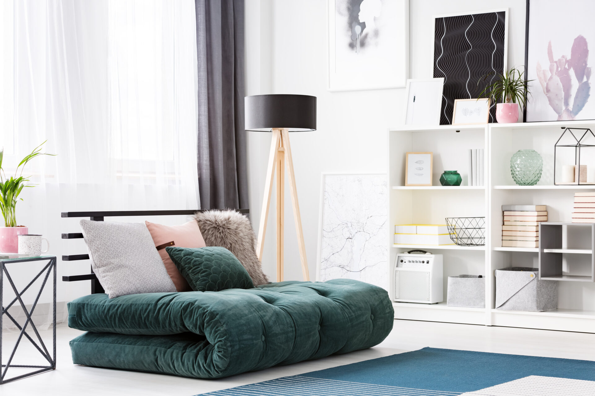 Cushions on green futon in modern bedroom interior with black wooden lamp and posters