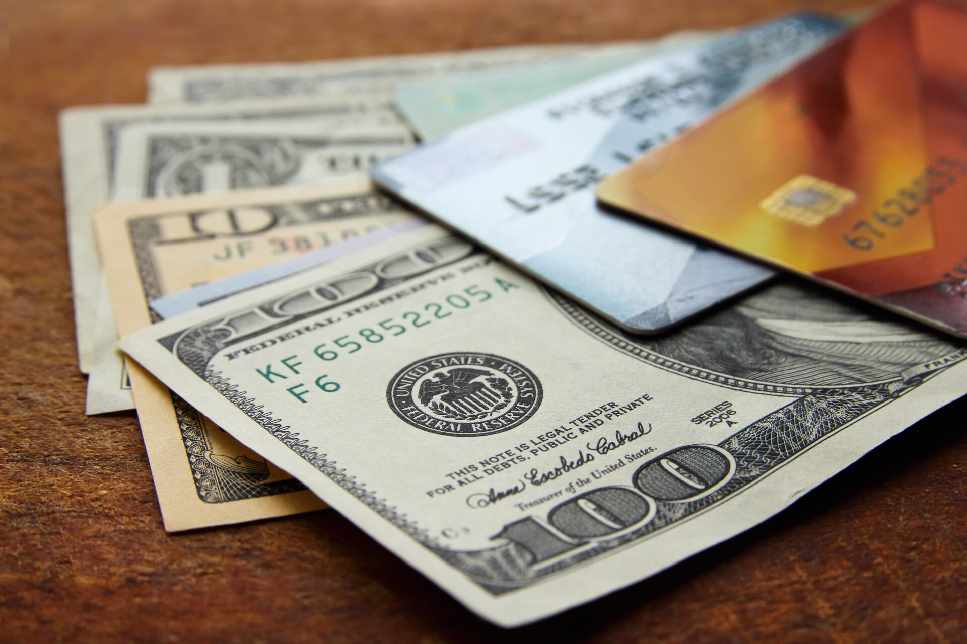 a few american dollar bills and plastic credit cards with chip on wooden background, close-up with selective focus.