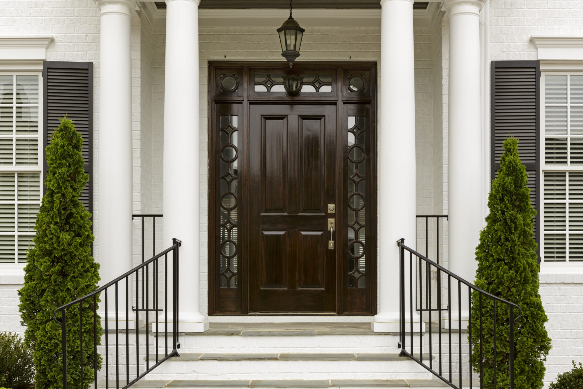 A grand entrance way leading up to an ornate dark wood door with green trees.