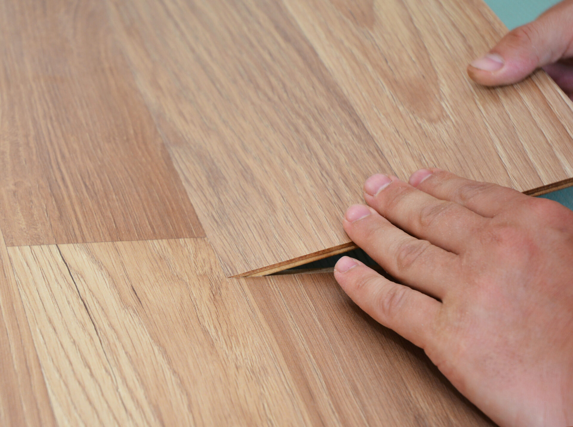 A close-up on a handyman, DYIer installing floating laminate floor, wood laminate flooring plank of natural oak or maple color on a padded underlayment, subfloor.