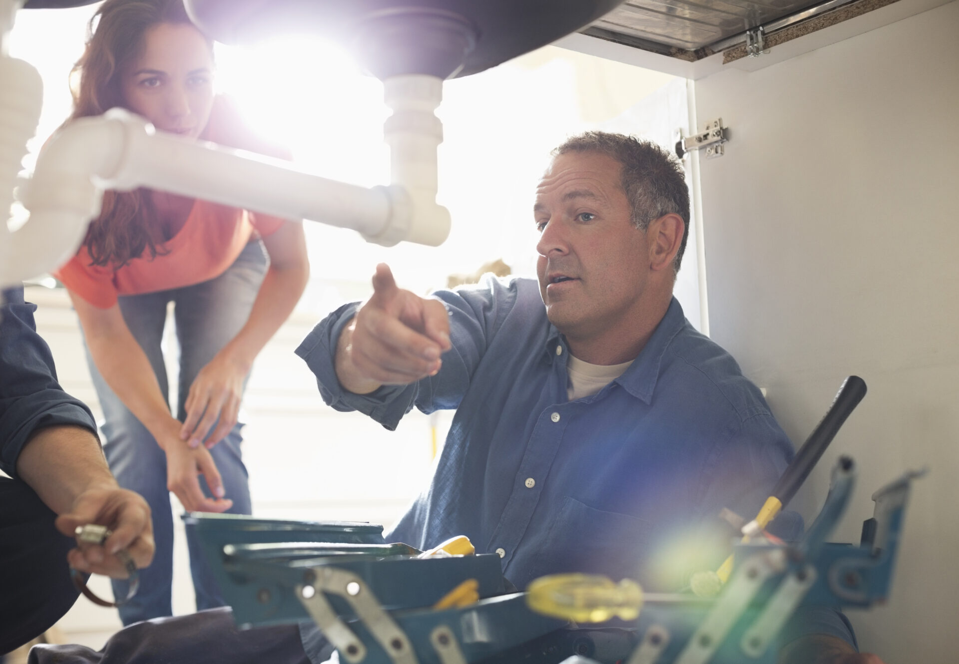 Plumbers working on pipes under sink