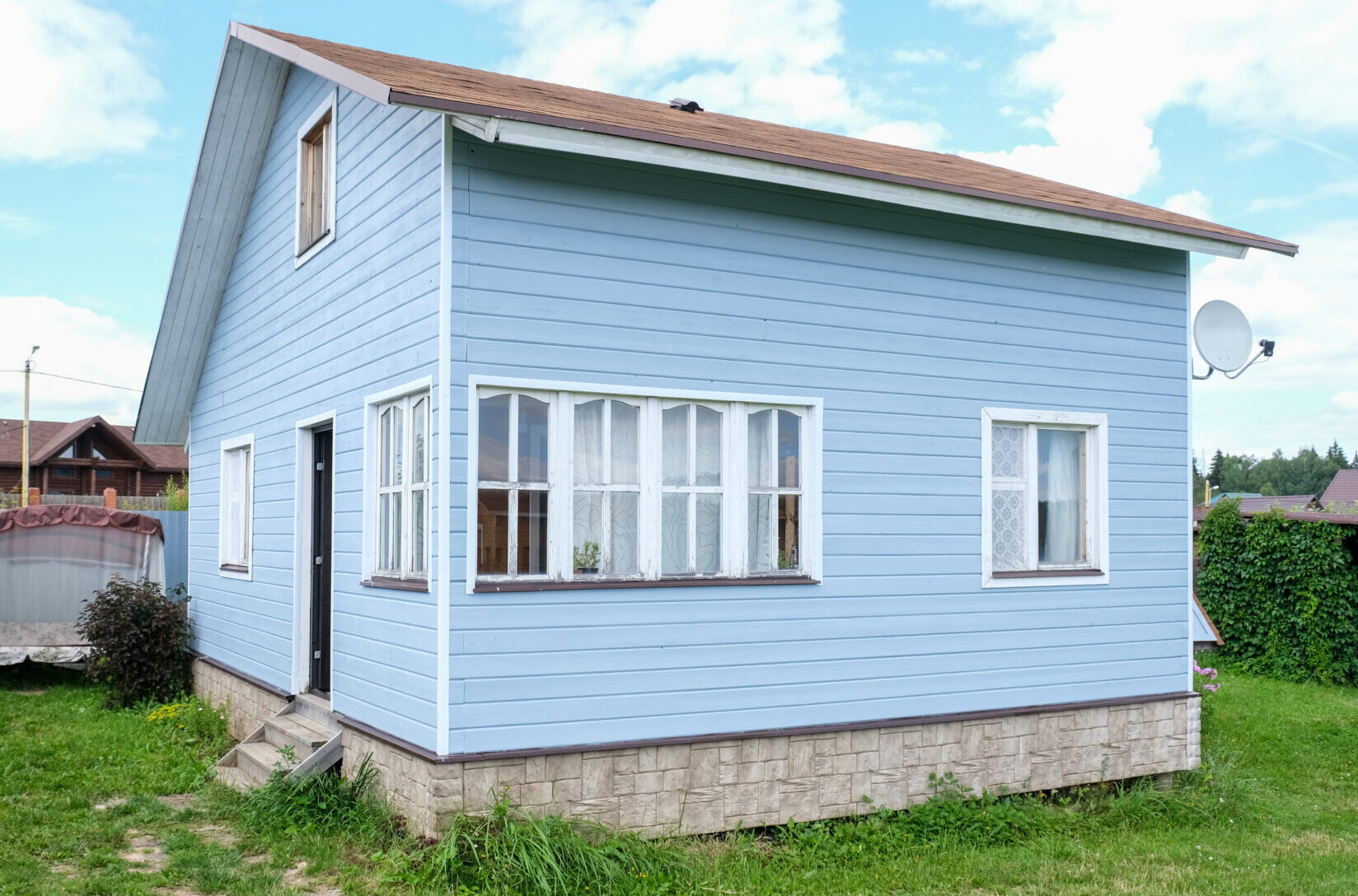 Small tiny wooden frame house painted in blue and white windows and door as a country residence in sunny summer day.