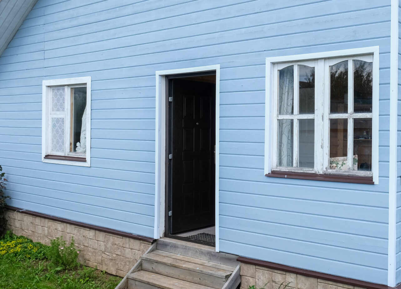 White windows of a small tiny frame house with blue walls,a country residence in sunny summer day.