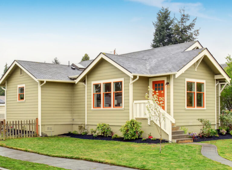 Old small green American home with porch. Green lawn around and driveway